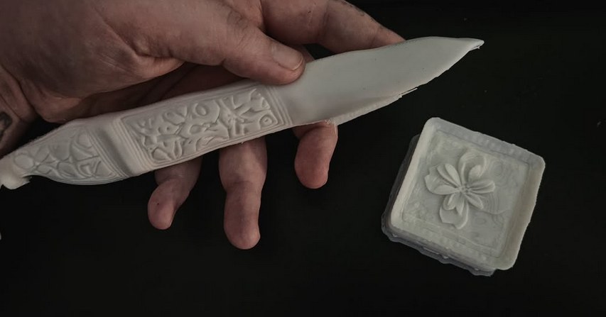 3D-printed knife and plaque held in hand, unpainted